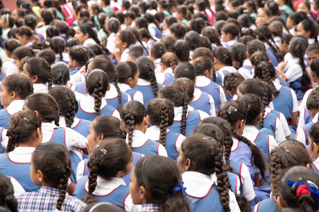 A gathering of schoolgirls in uniforms with neatly braided hair, viewed from behind.